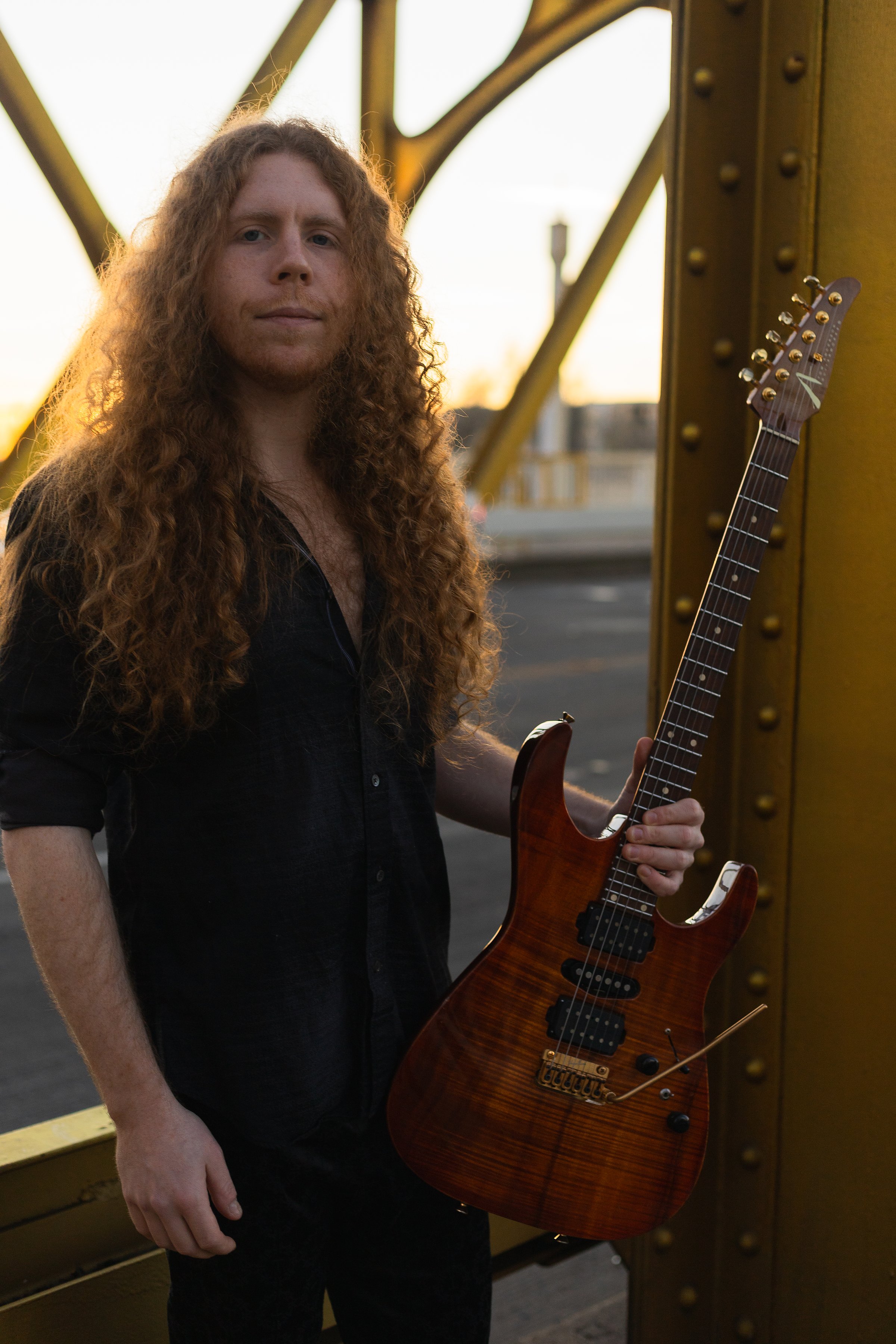 Sean Ashe standing with an electric guitar on Sacramento’s Tower Bridge at golden hour.
