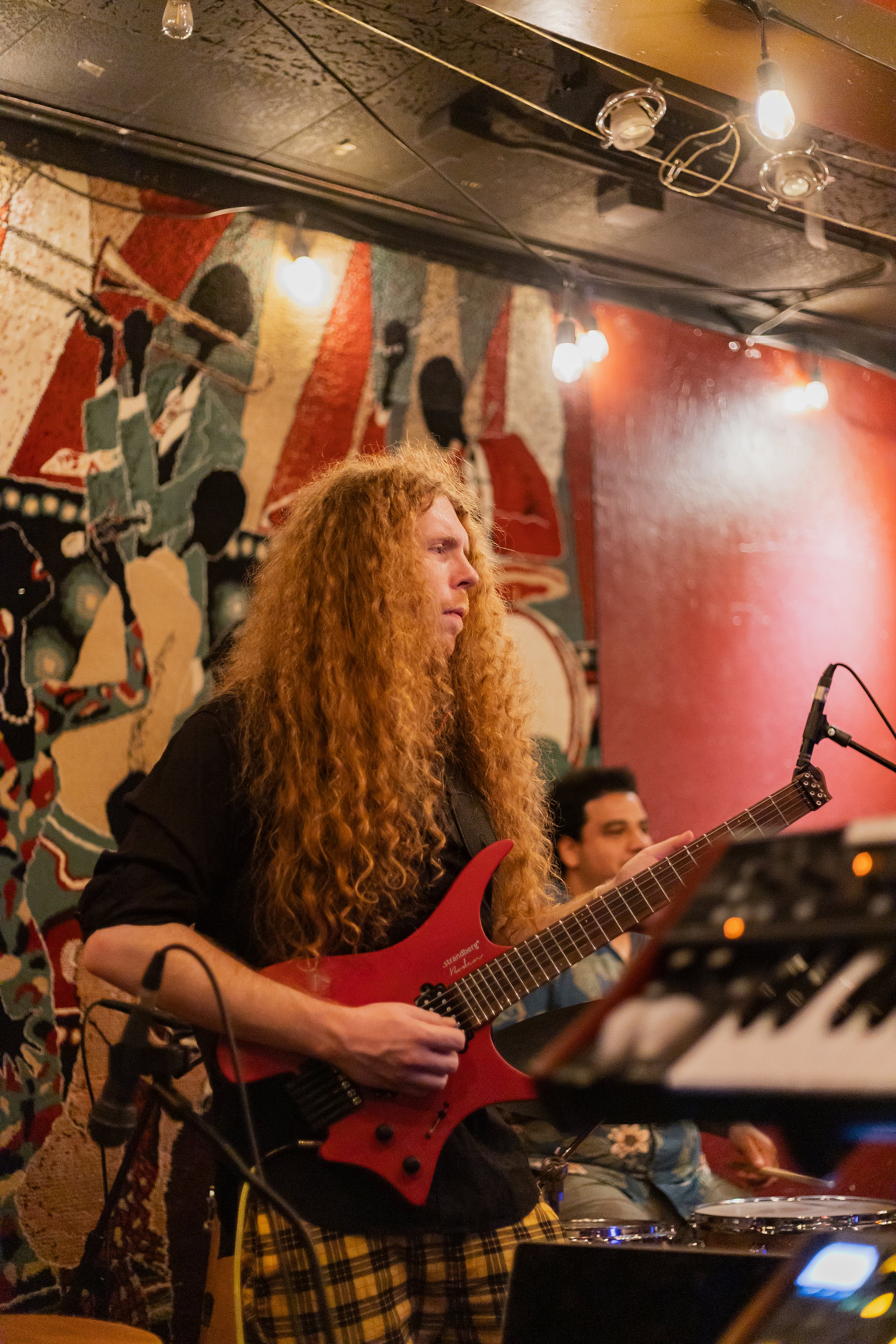 Sean Ashe playing a red electric guitar during a live performance at the Torch Club.