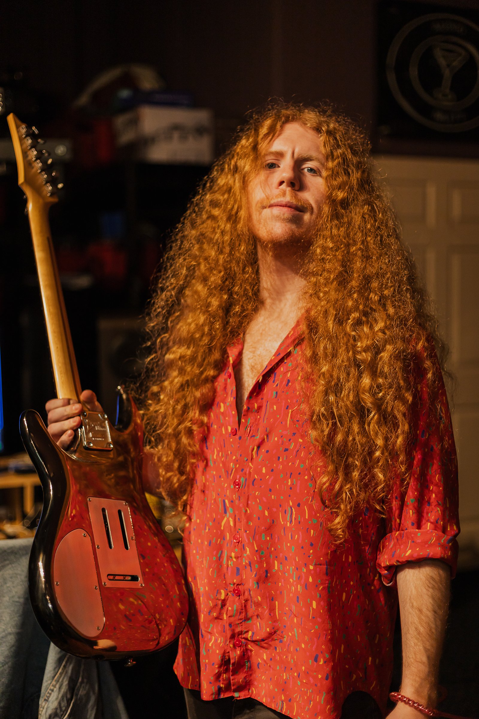 Sean Ashe holding an electric guitar in a warmly lit recording studio.