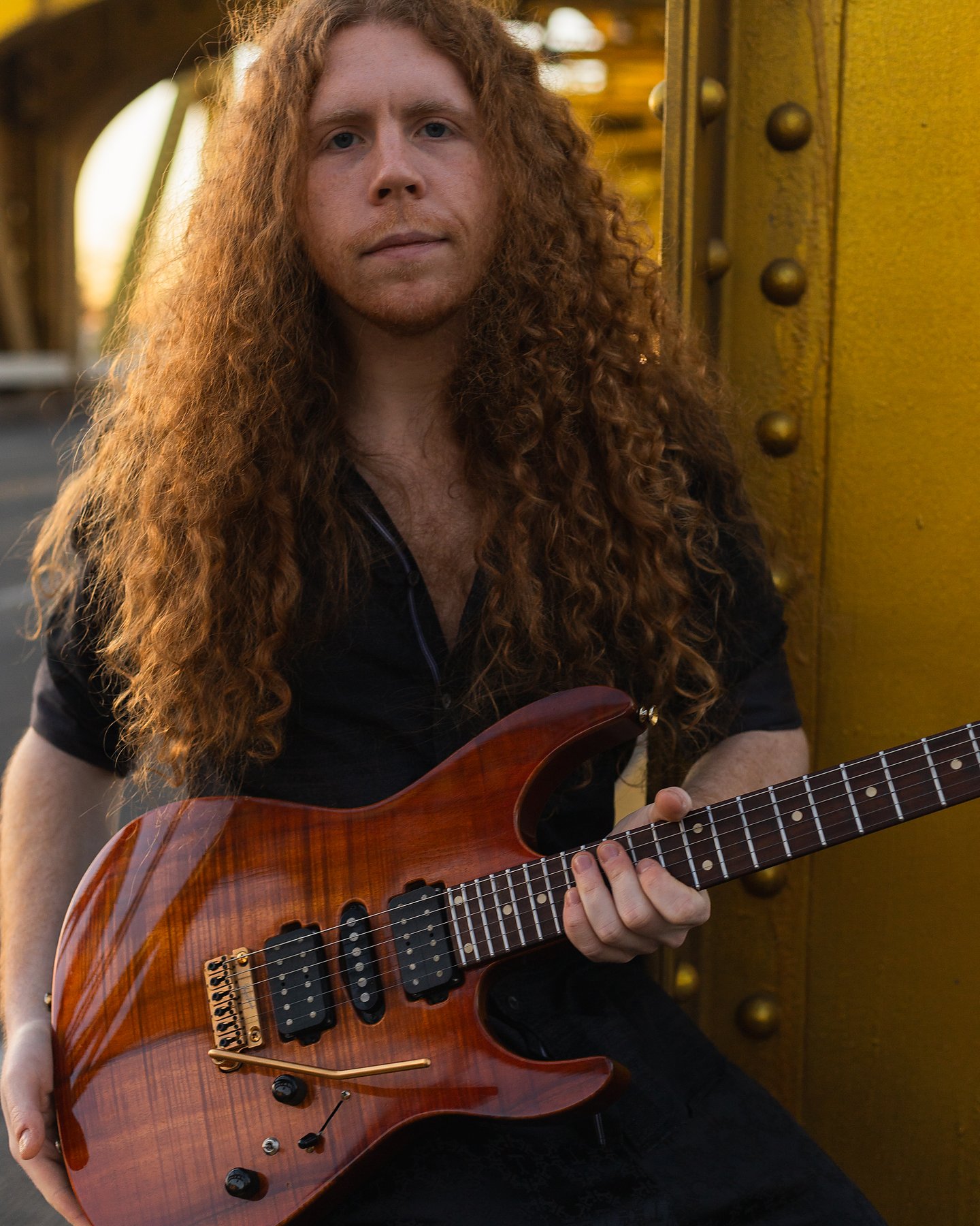 Sean Ashe holding a natural-finish electric guitar beside Sacramento’s yellow Tower Bridge.