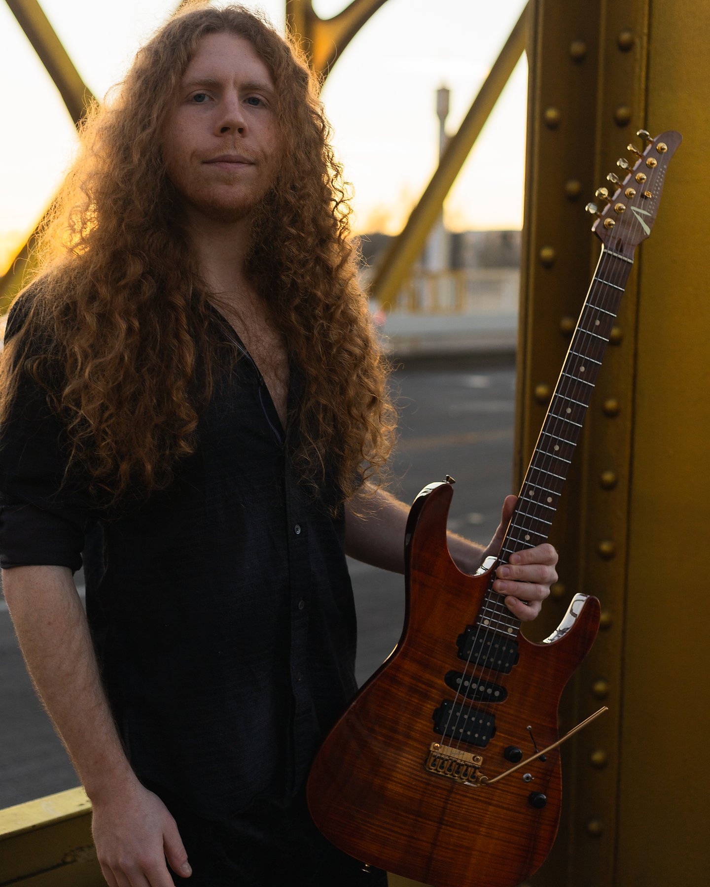 Sean Ashe standing with an electric guitar on Sacramento’s Tower Bridge at golden hour.