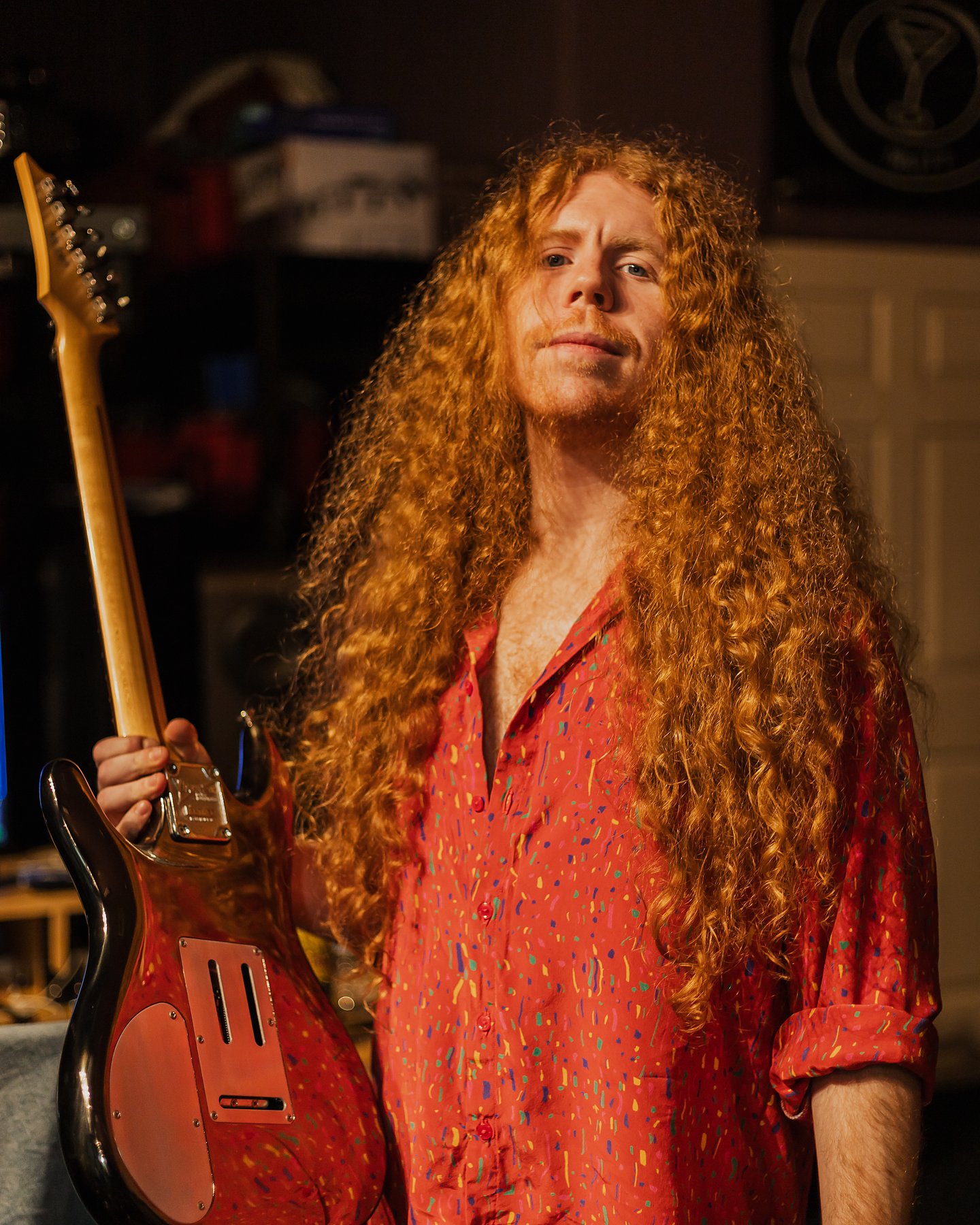 Sean Ashe holding an electric guitar in a warmly lit recording studio.